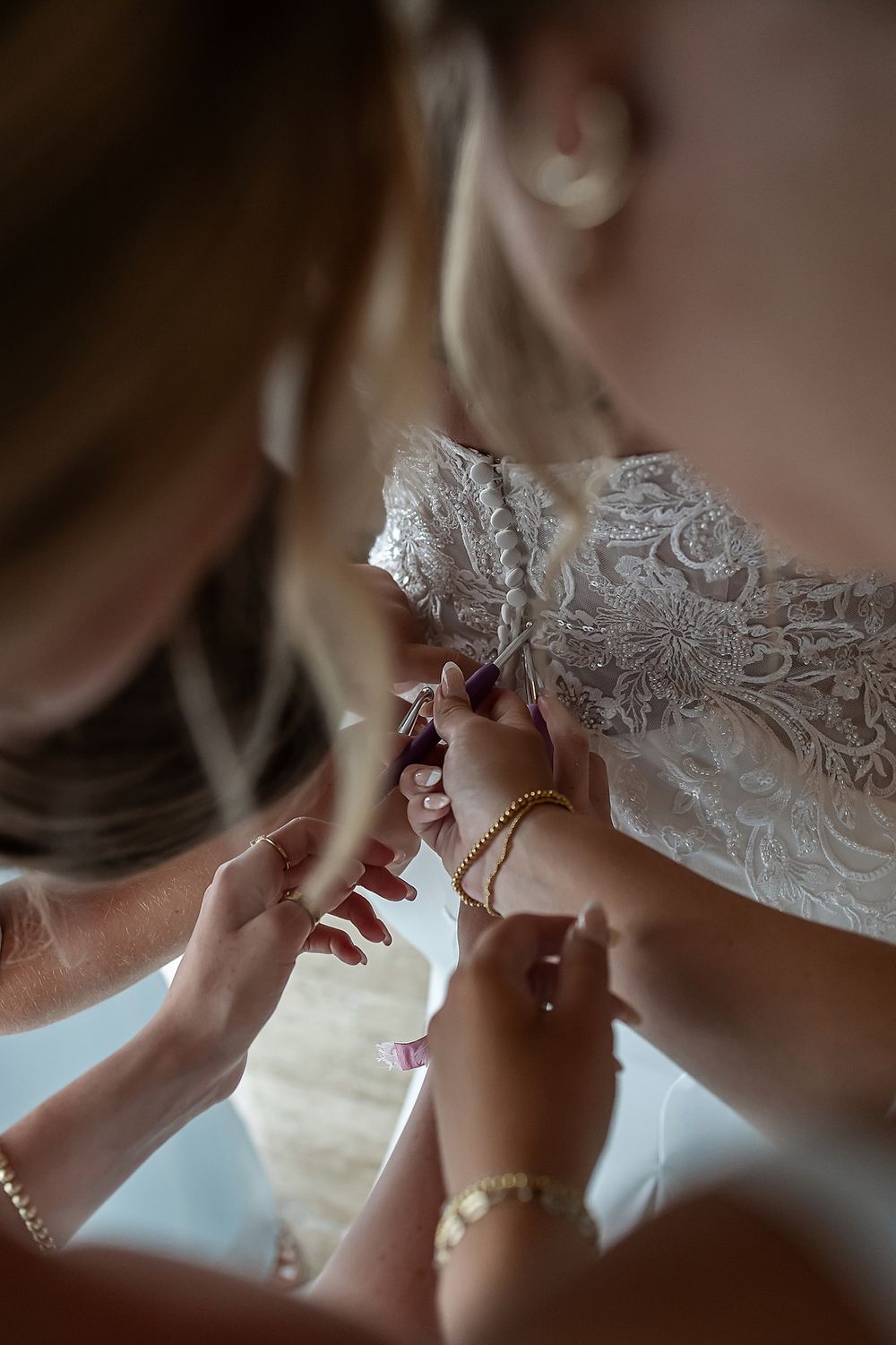 Close-up shots of someone adjusting white lace details on a wedding dress in soft morning light.