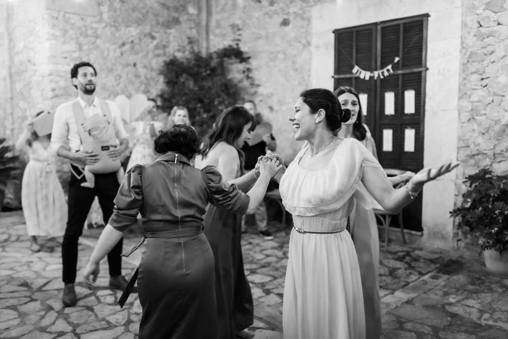 Schwarz-Weiß-Fotografie von Menschen, die gemeinsam auf einer Hochzeitsfeier im Freien auf einer Steinterrasse tanzen.