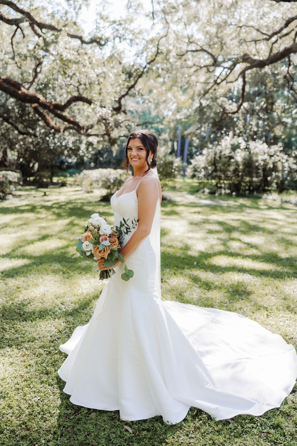 Beautiful spring wedding portrait under blooming white cherry blossoms with flowing mermaid dress and bridal bouquet.