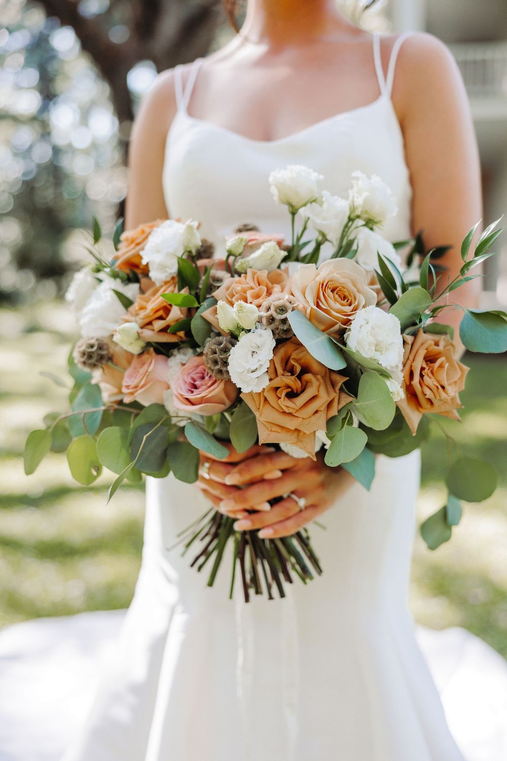 Three coordinated bridal bouquets featuring peach and white roses with eucalyptus greenery against a bright outdoor setting.