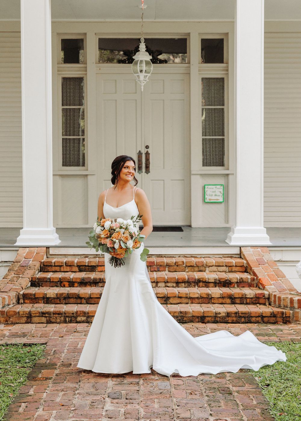 Elegant white wedding dress with fitted silhouette and train photographed on historic brick steps of southern style home.
