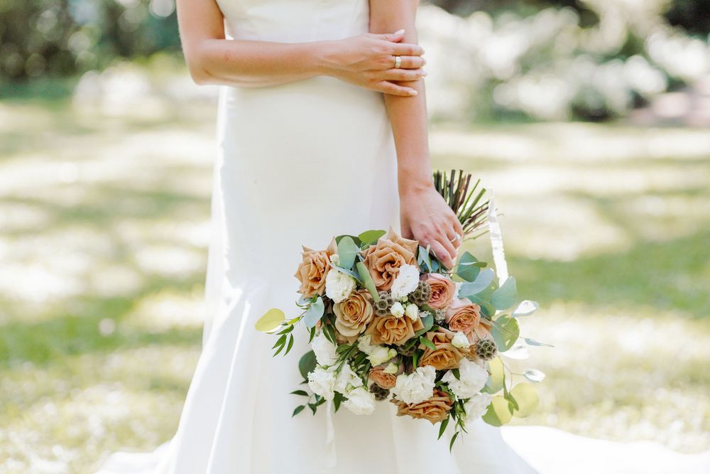 A beautiful wedding bouquet with peach and coral flowers mixed with eucalyptus held against a white wedding dress.