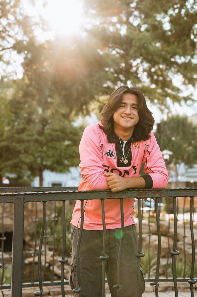 Person in pink jacket leans on metal railing during golden hour with sun flare in background.