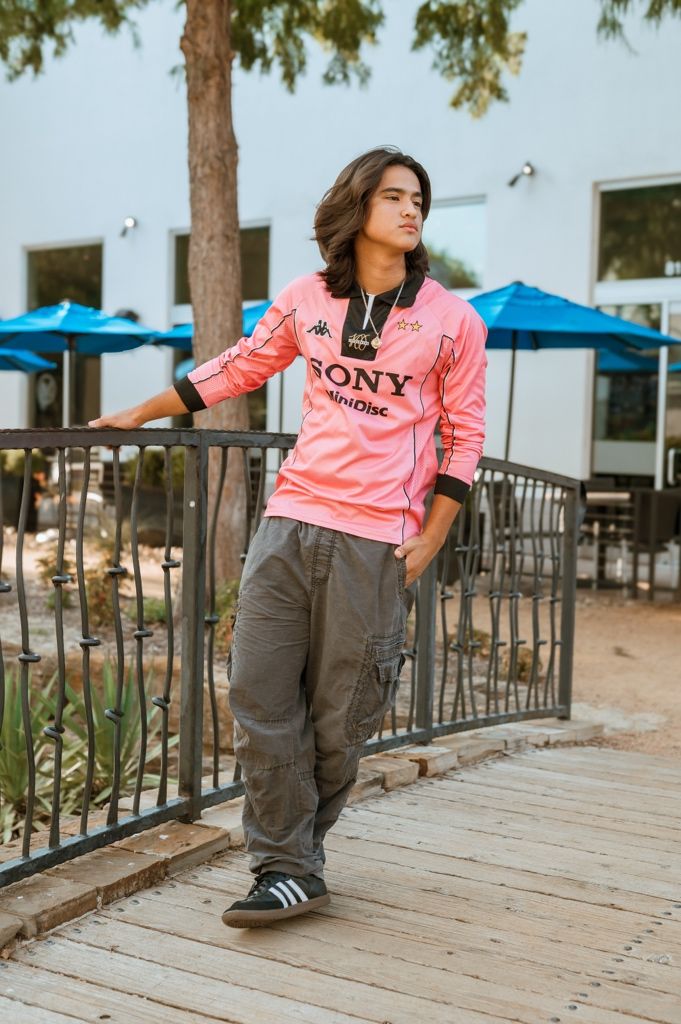 Person wearing pink sweatshirt and gray pants strikes dynamic poses on wooden deck with metal railing and trees in background.