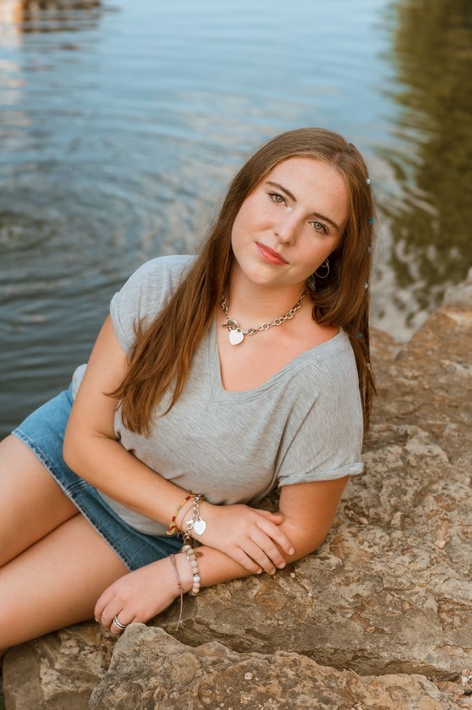 A person in a gray t-shirt and denim reclines on a rocky lakeside during a portrait session at golden hour.