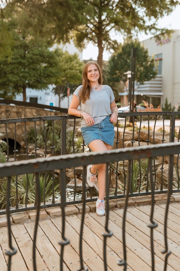 Casual summer outfit featuring a gray t-shirt and denim skirt styled with white sneakers on an outdoor wooden deck.