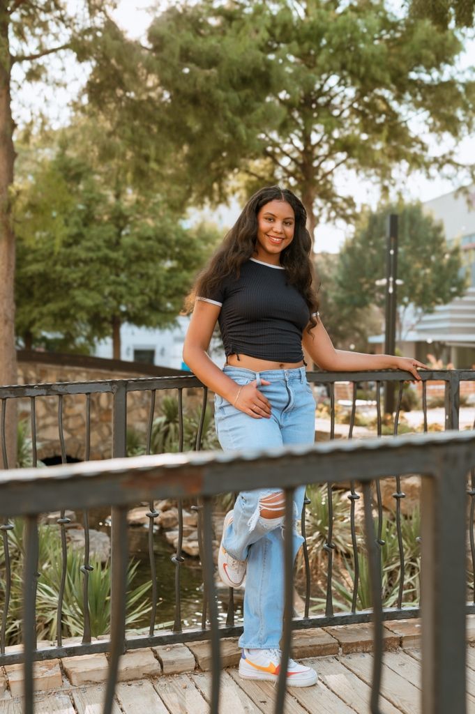 A casual summer outfit with ripped jeans and black crop top on a wooden deck with trees in the background.
