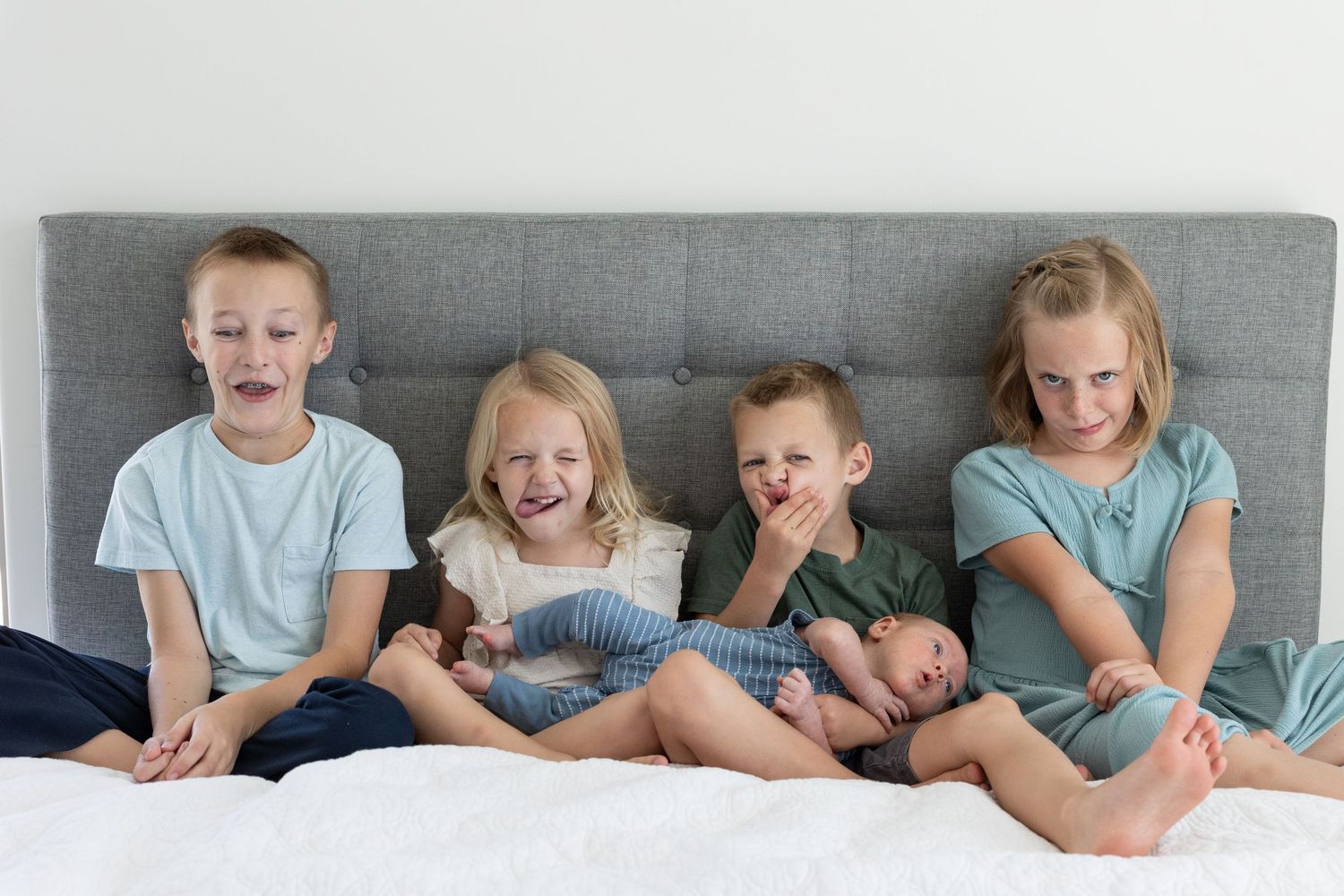 5 kids sitting on bed making silly faces at the camera