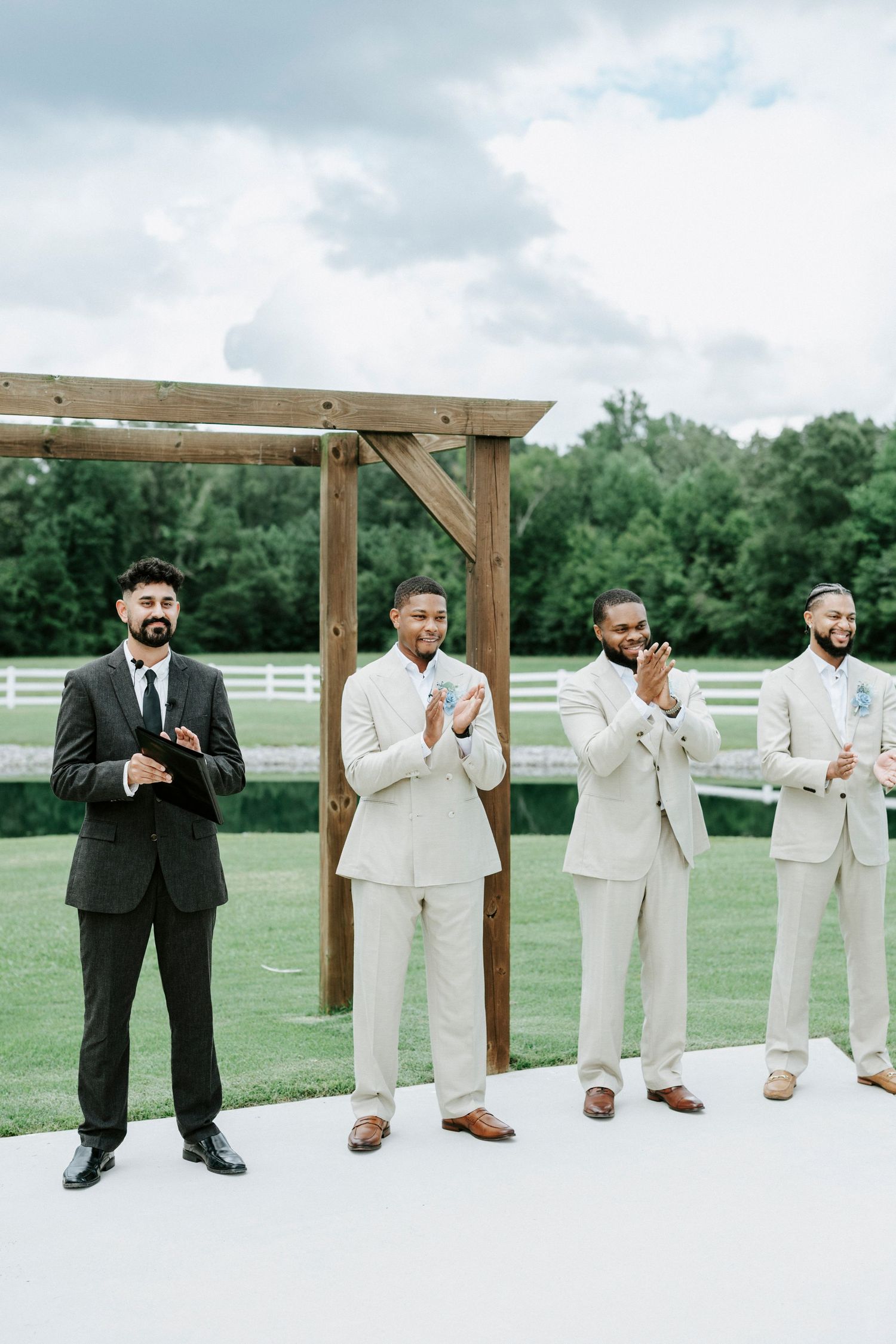 Four groomsmen stand at wooden altar during outdoor wedding ceremony.