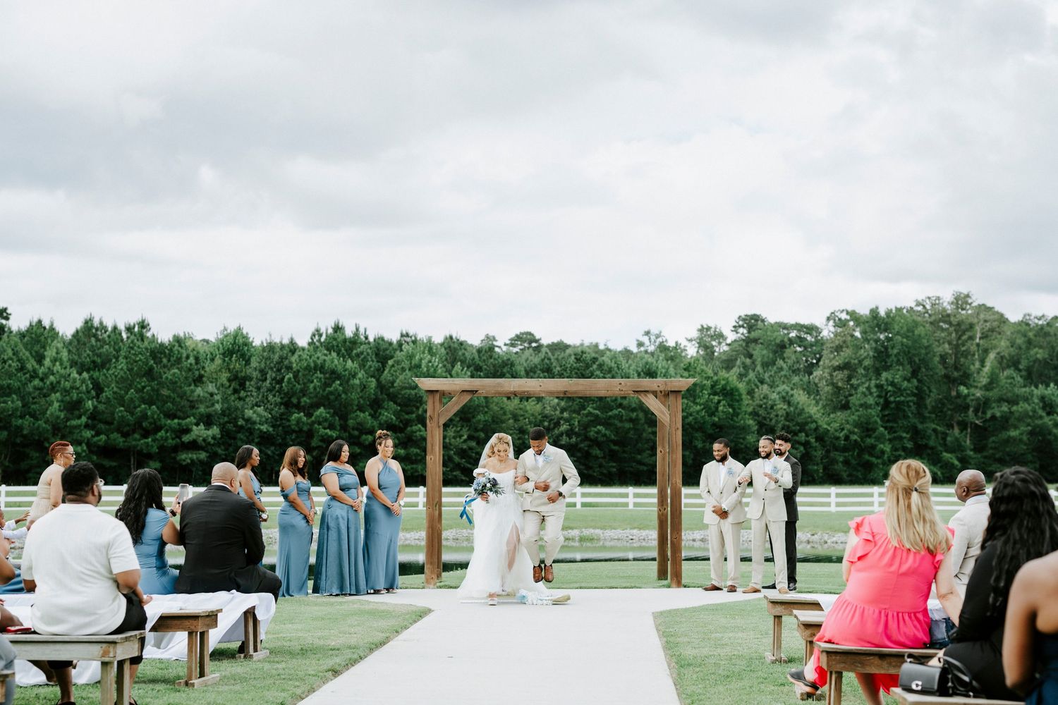 Rustic outdoor wedding ceremony with wooden arbor and guests seated on benches.