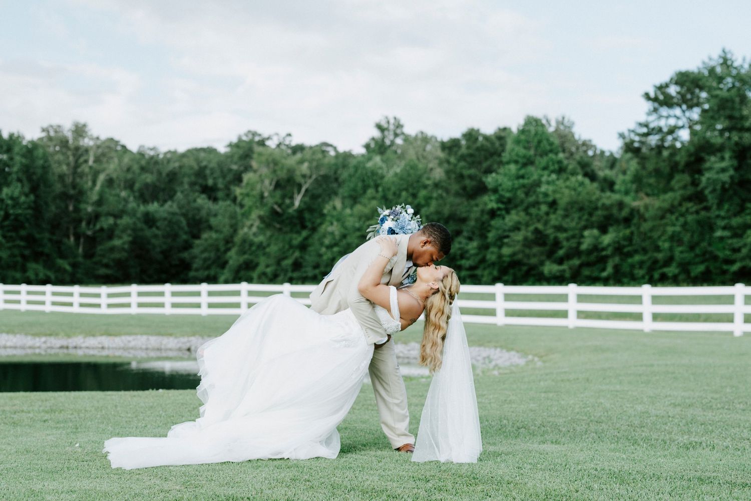 Couple shares romantic dip pose during wedding photoshoot on scenic grounds.