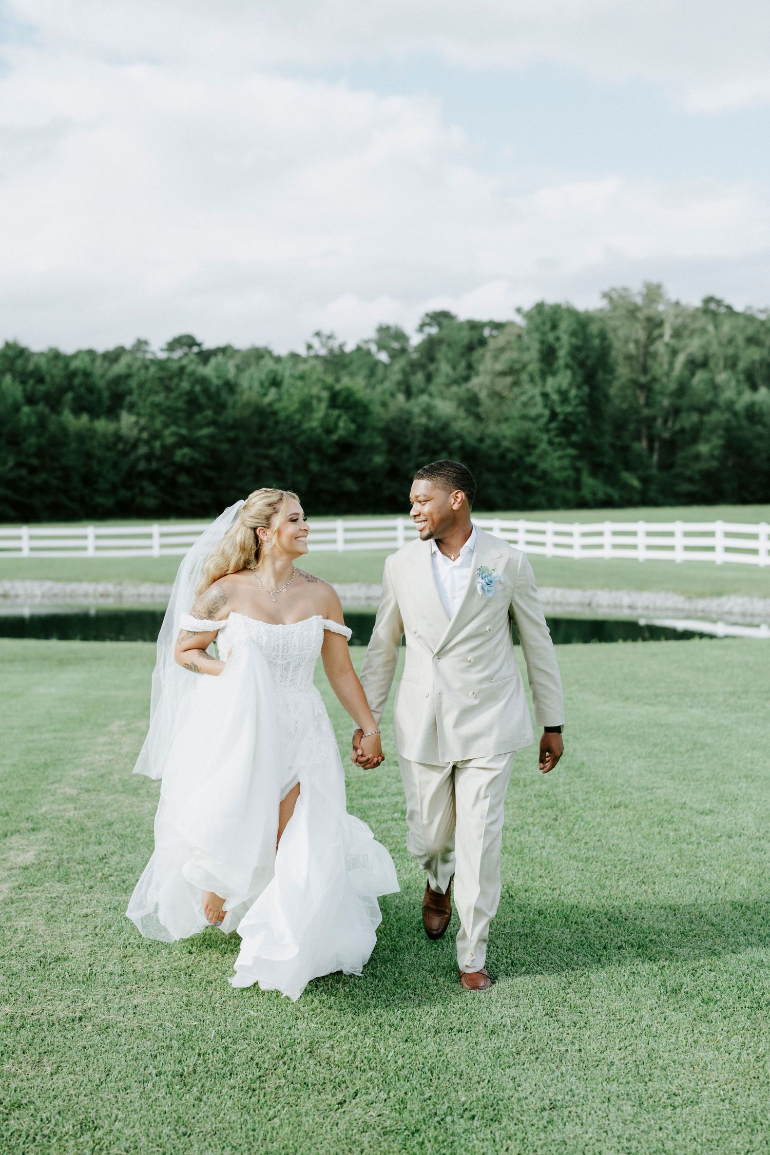 Newlyweds walking hand in hand on grass with bride's dress flowing in the breeze.