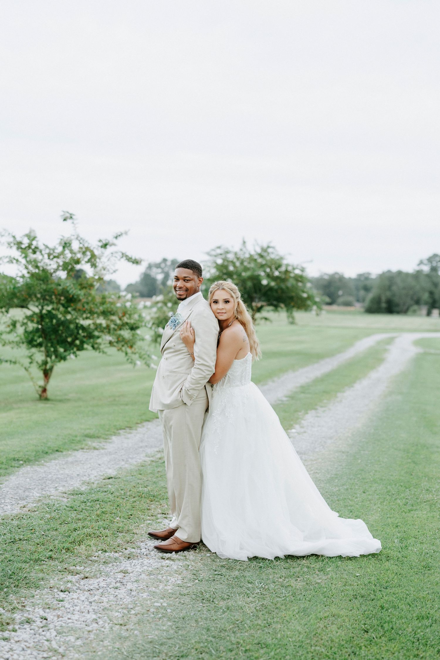 A romantic wedding photoshoot captured in a serene outdoor setting with a gravel path and green landscape.