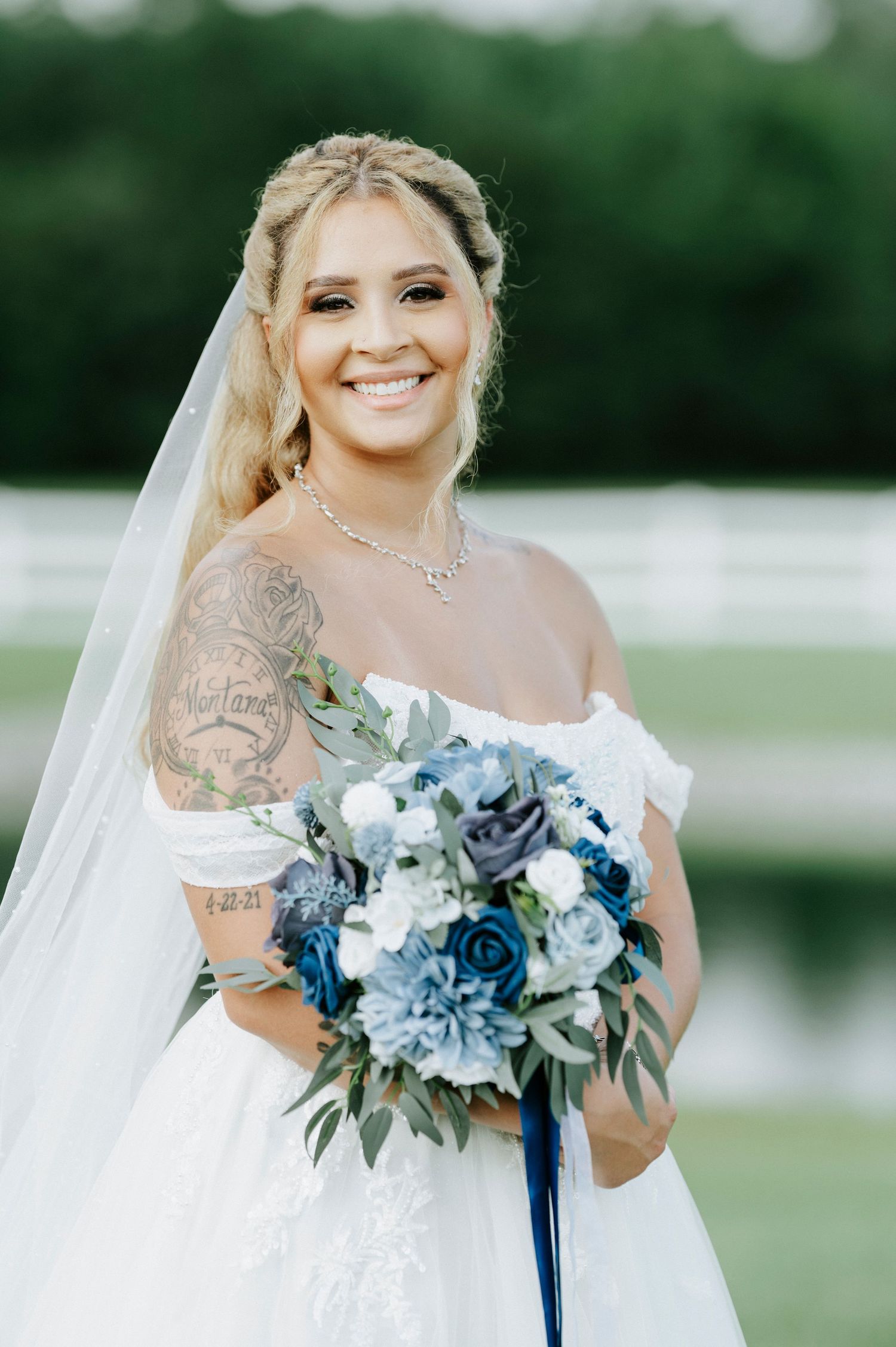 Bridal bouquet featuring blue and white flowers with cascading ribbons against a natural backdrop.