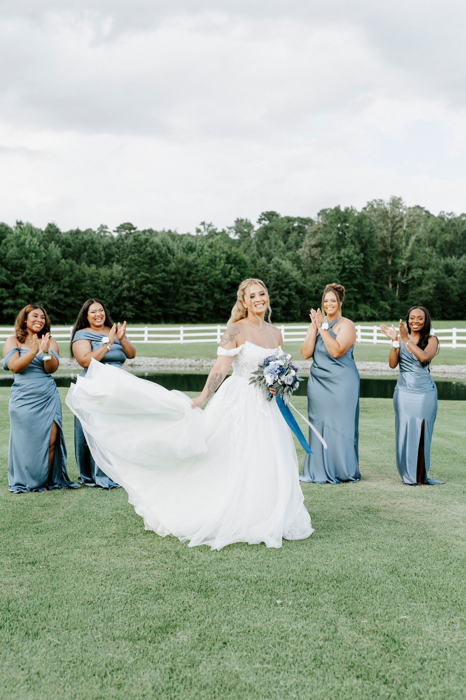 Bridesmaids in blue dresses helping the bride with her dress during outdoor photo session.