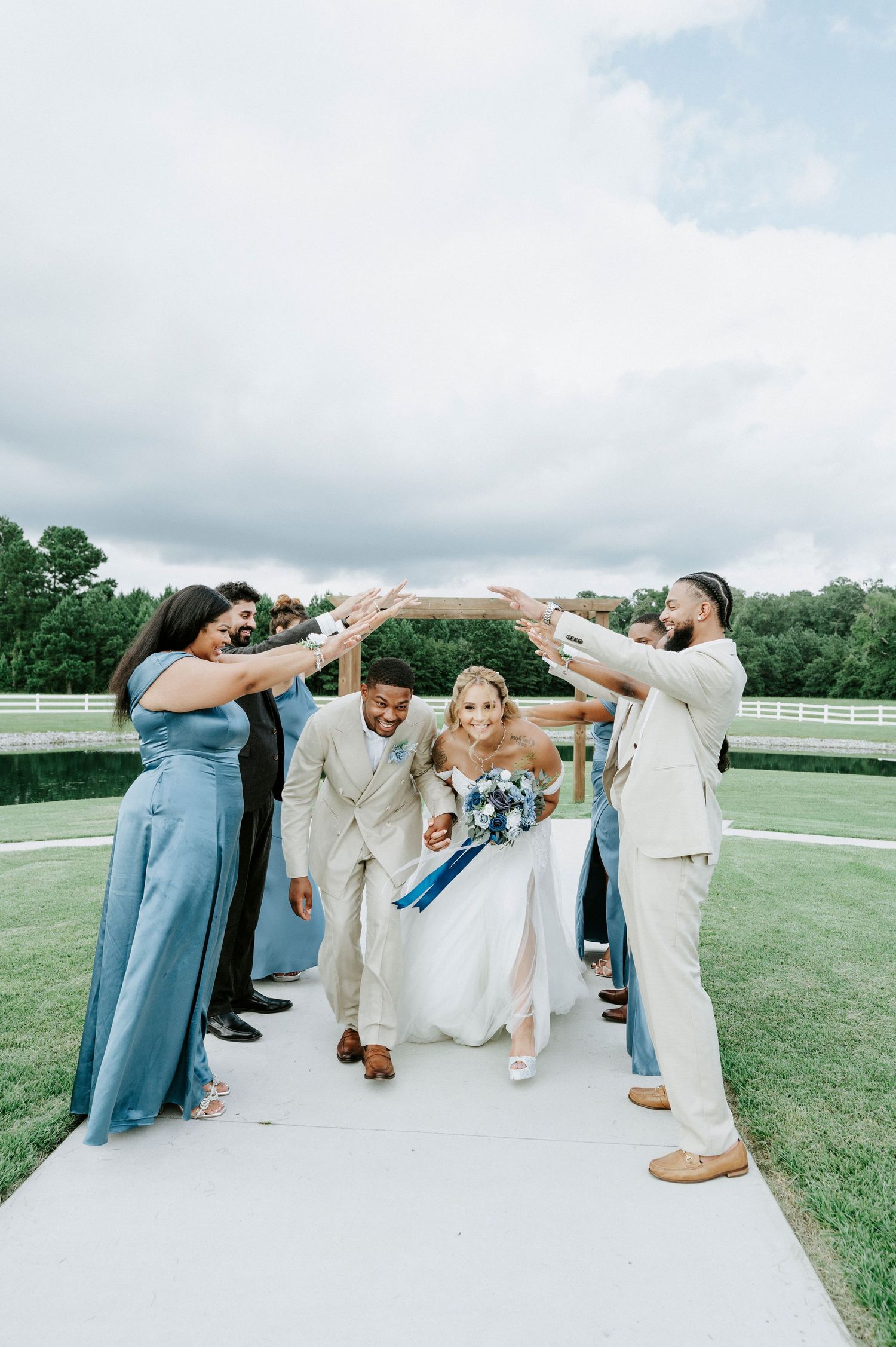 Wedding party forms a tunnel for the newlyweds to walk through on grassy field.