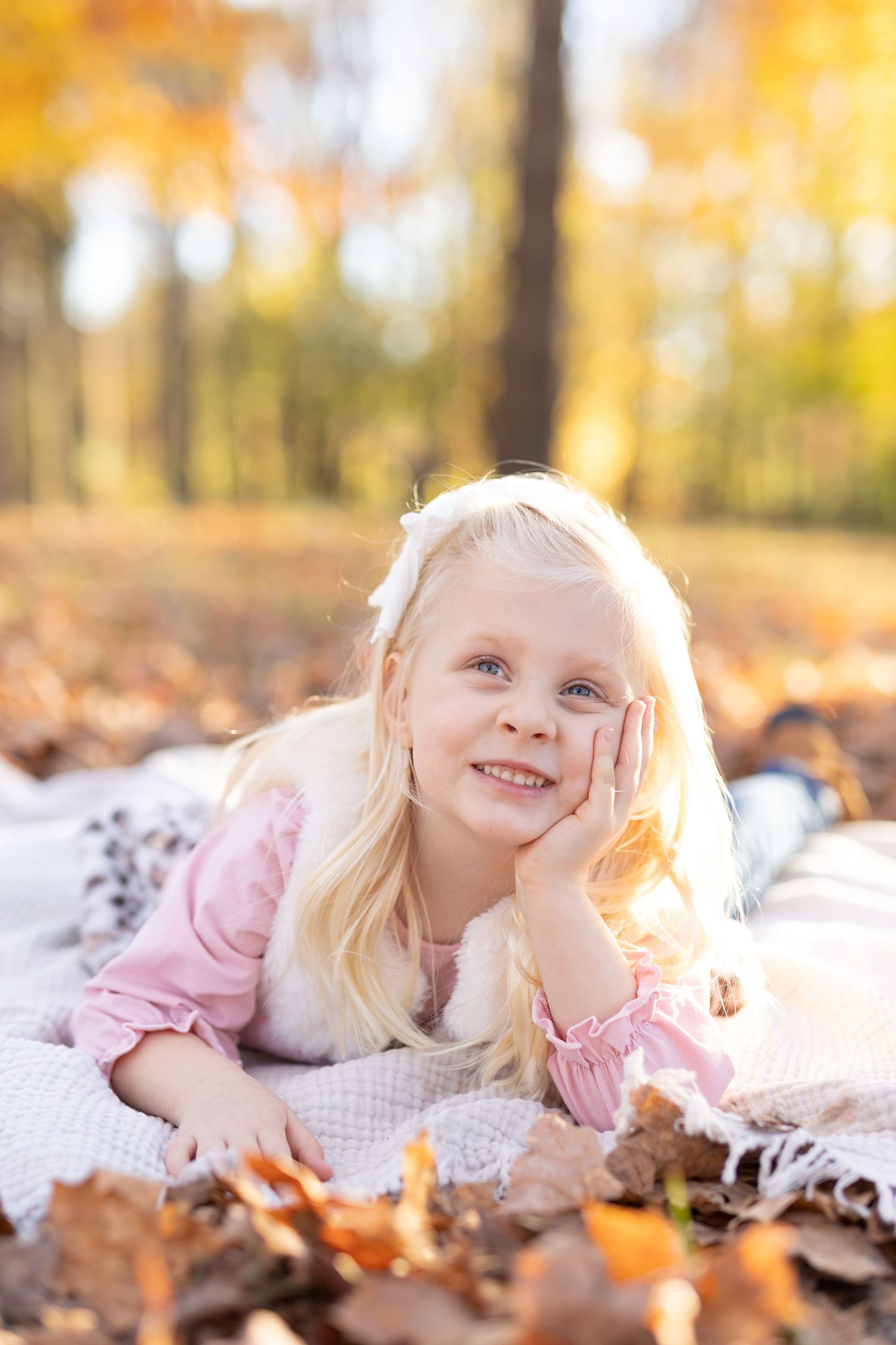 Smiling blonde-haired girl lying on a blanket in a bed of fall leaves