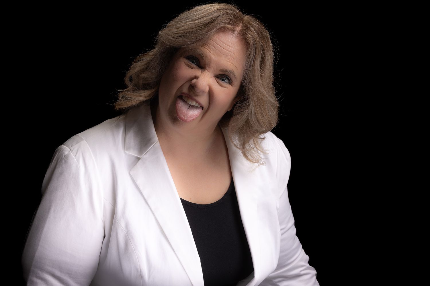 Professional studio portrait of a person in a white blazer and black top against a dark background.