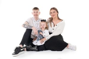 Family wearing coordinated white and black outfits sitting together on floor against white background for portrait session.