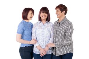 Three people wearing casual patterned shirts standing close together and smiling against a white background.