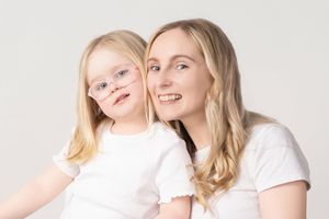 Candid portrait of loving parent and child in white shirts smiling together against light background.