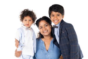 Three individuals pose together smiling warmly at the camera, wearing casual and formal attire.