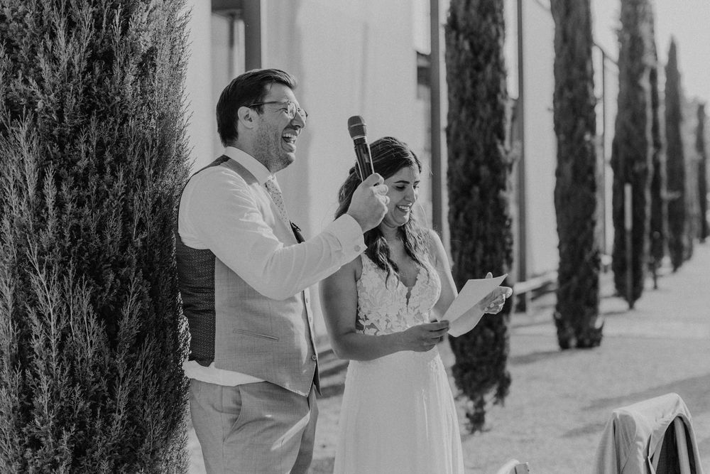 Das Brautpaar hält eine Rede zum Start des Dinners am Hochzeitstag, der hält das Mikrofon und lacht.