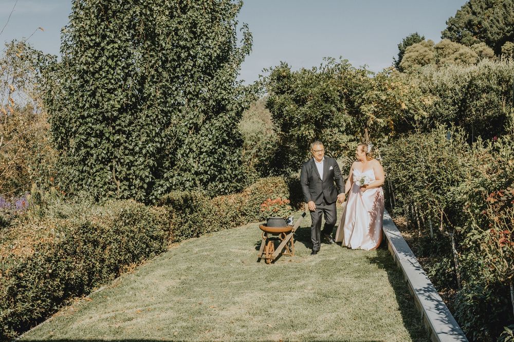A couple and their dog walk through a lush garden path on a sunny summer day.