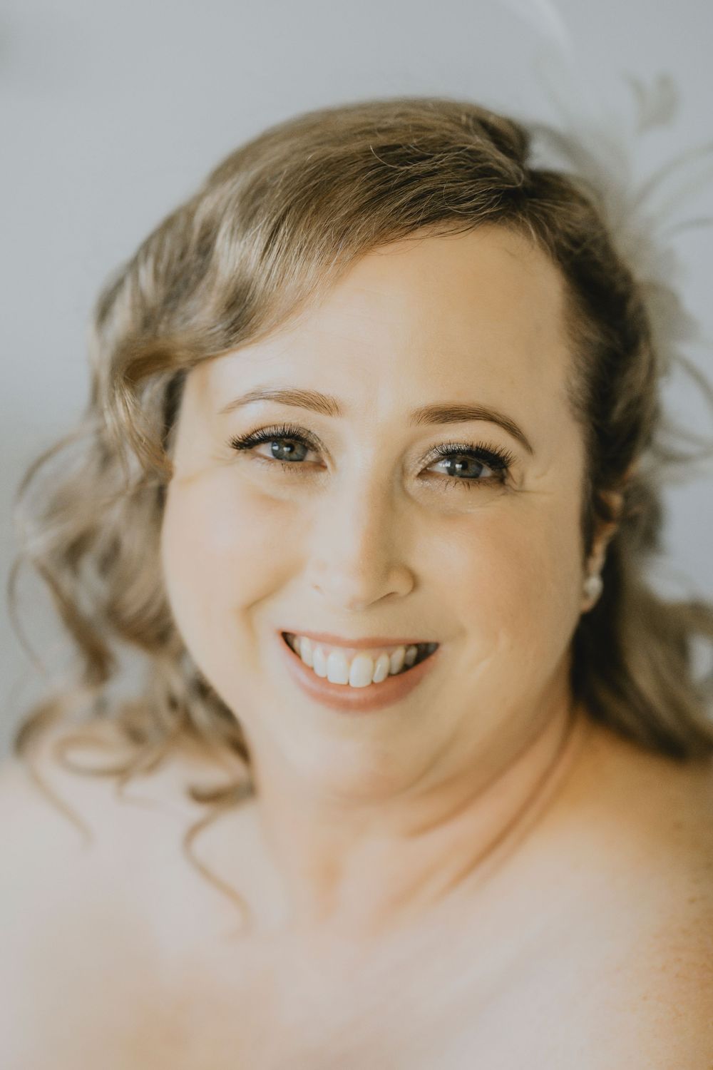 A close-up professional portrait with soft lighting showing a warm genuine smile and wavy hair.