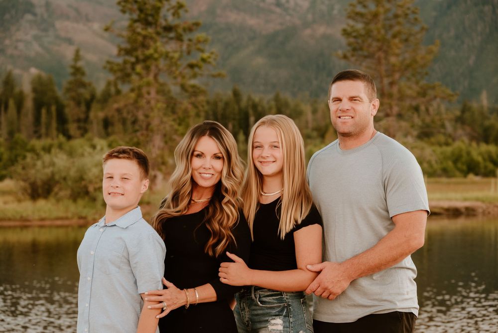A group poses outdoors during golden hour near a lake with mountains and autumn trees in the background.