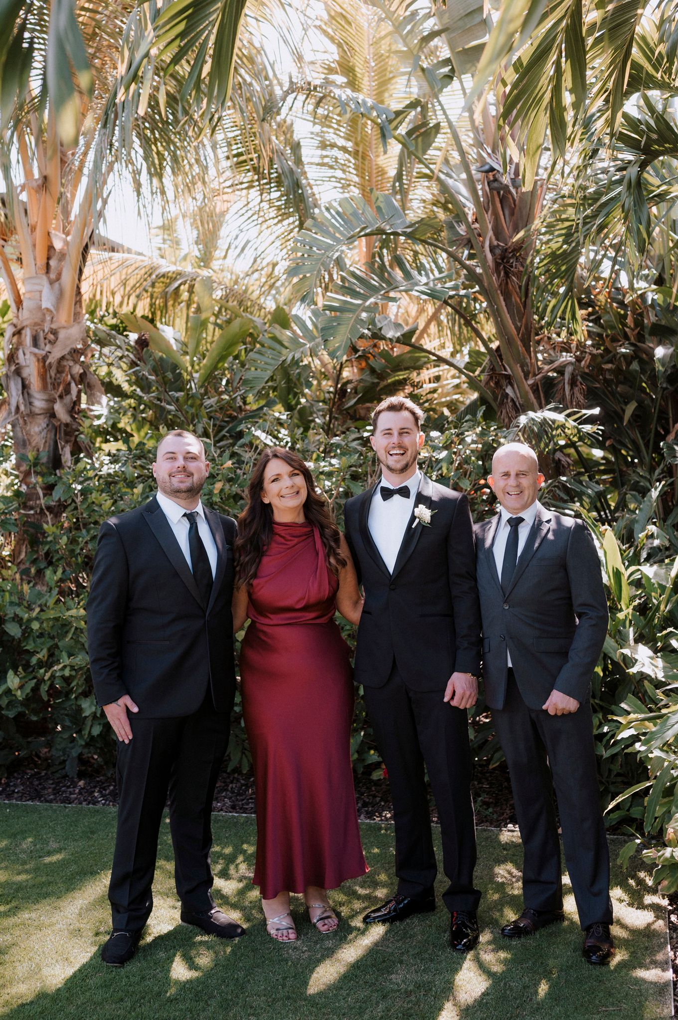 Four people in formal attire pose for a group photo against a backdrop of tropical palm trees.