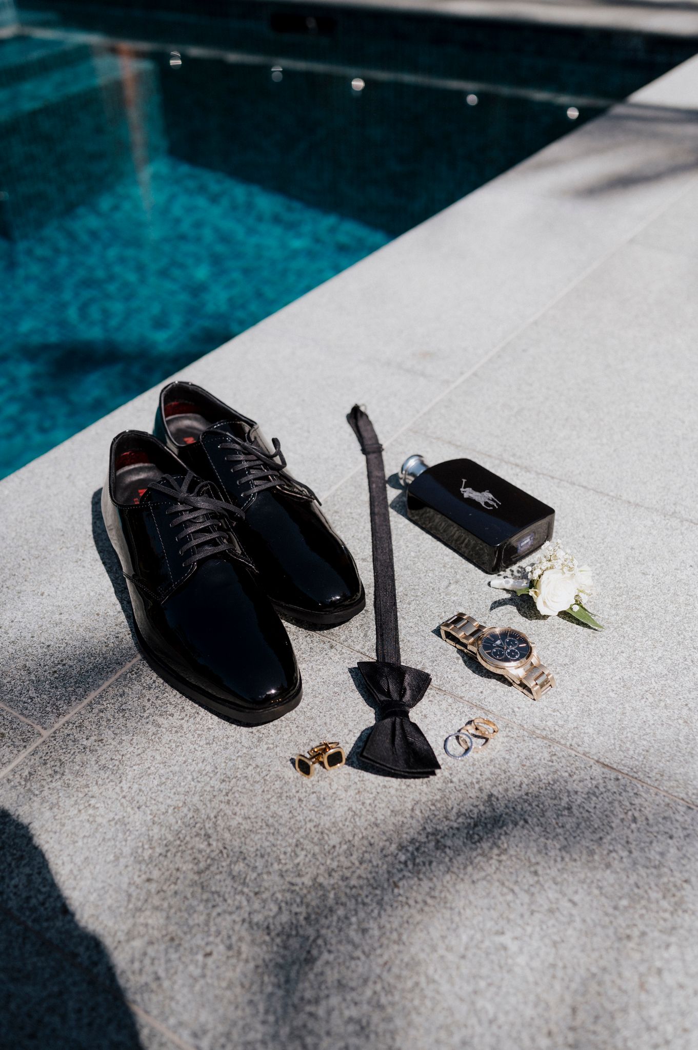 Groom's formal shoes and accessories arranged by a luxurious pool edge.