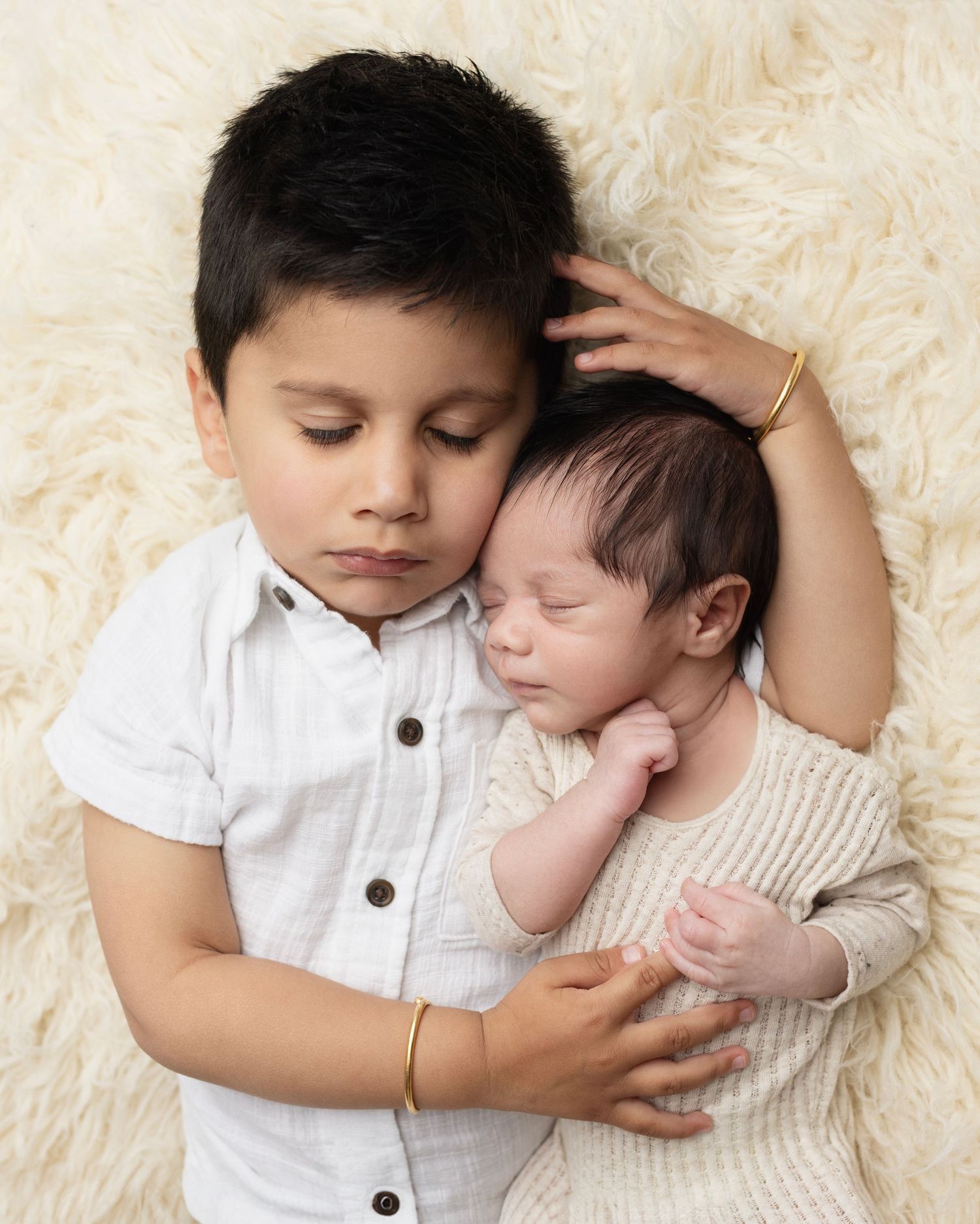 Sibling portrait of young children in white and cream tones on plush rug.