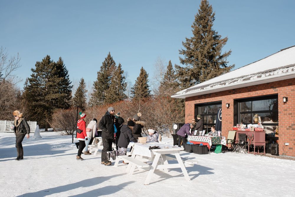 Winter scene at a ski resort with skiers and buildings nestled among snow-covered pine trees in the background.
