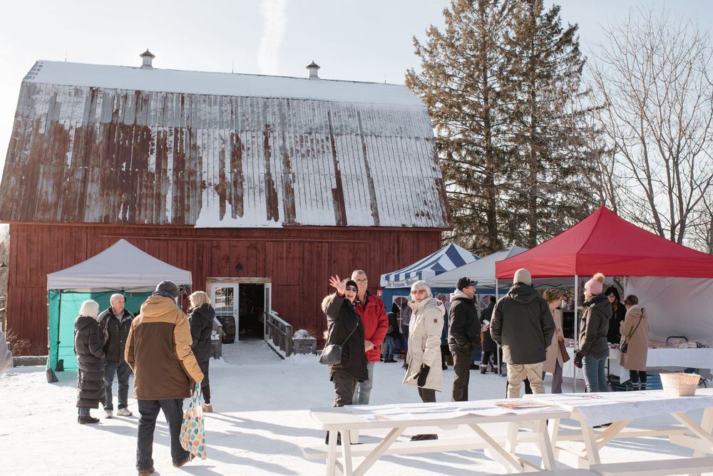 People enjoy winter activities at a snow-covered barn and farm setting during a seasonal outdoor gathering.