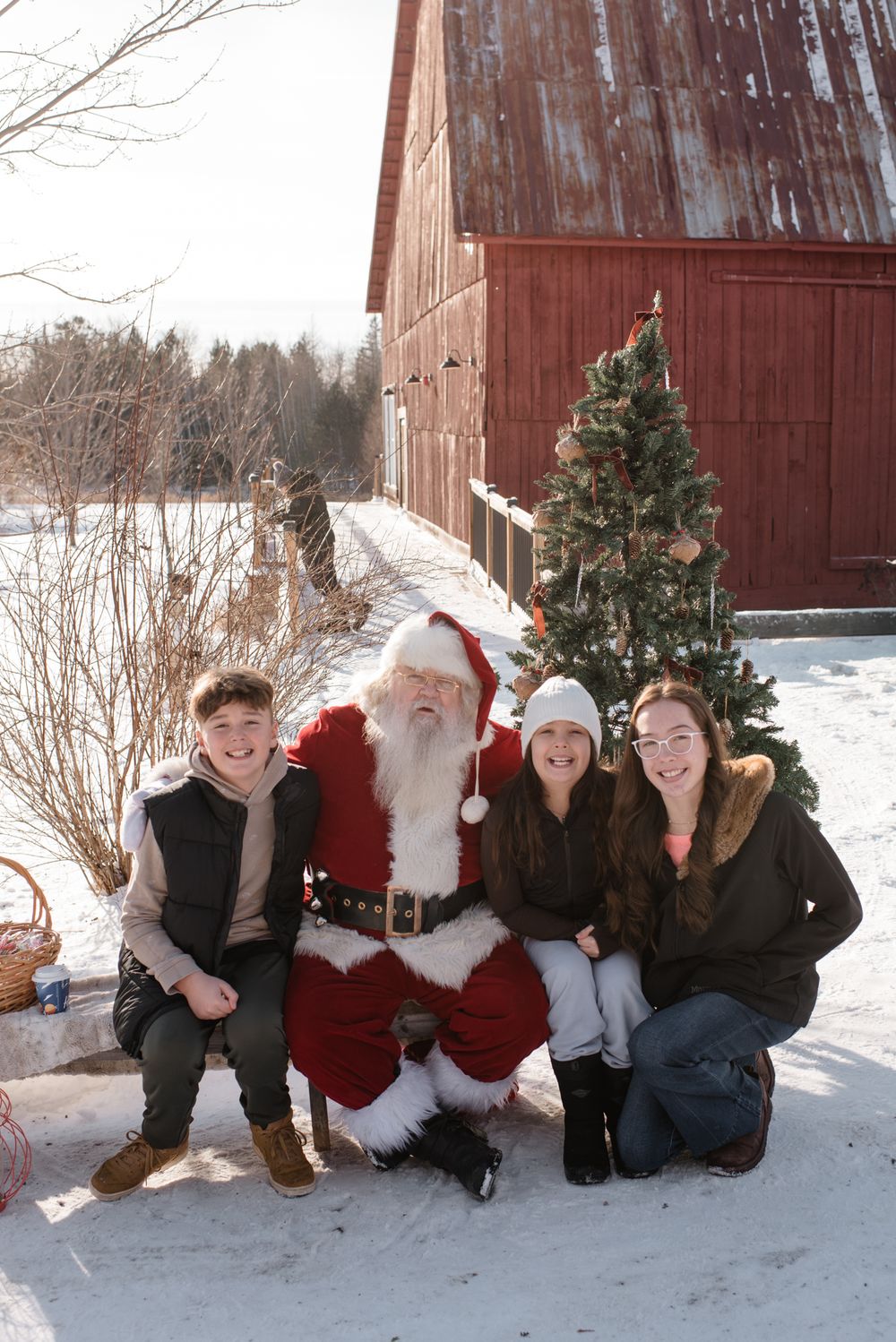 A group gathers in front of a rustic red barn during winter with snow-covered ground.