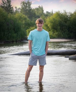 Person wading in shallow river water wearing blue shirt and shorts at sunset.