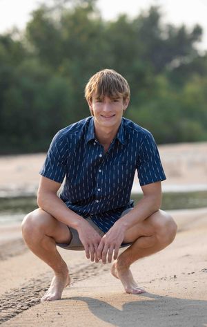 Person in navy striped shirt crouching on sandy beach at golden hour.