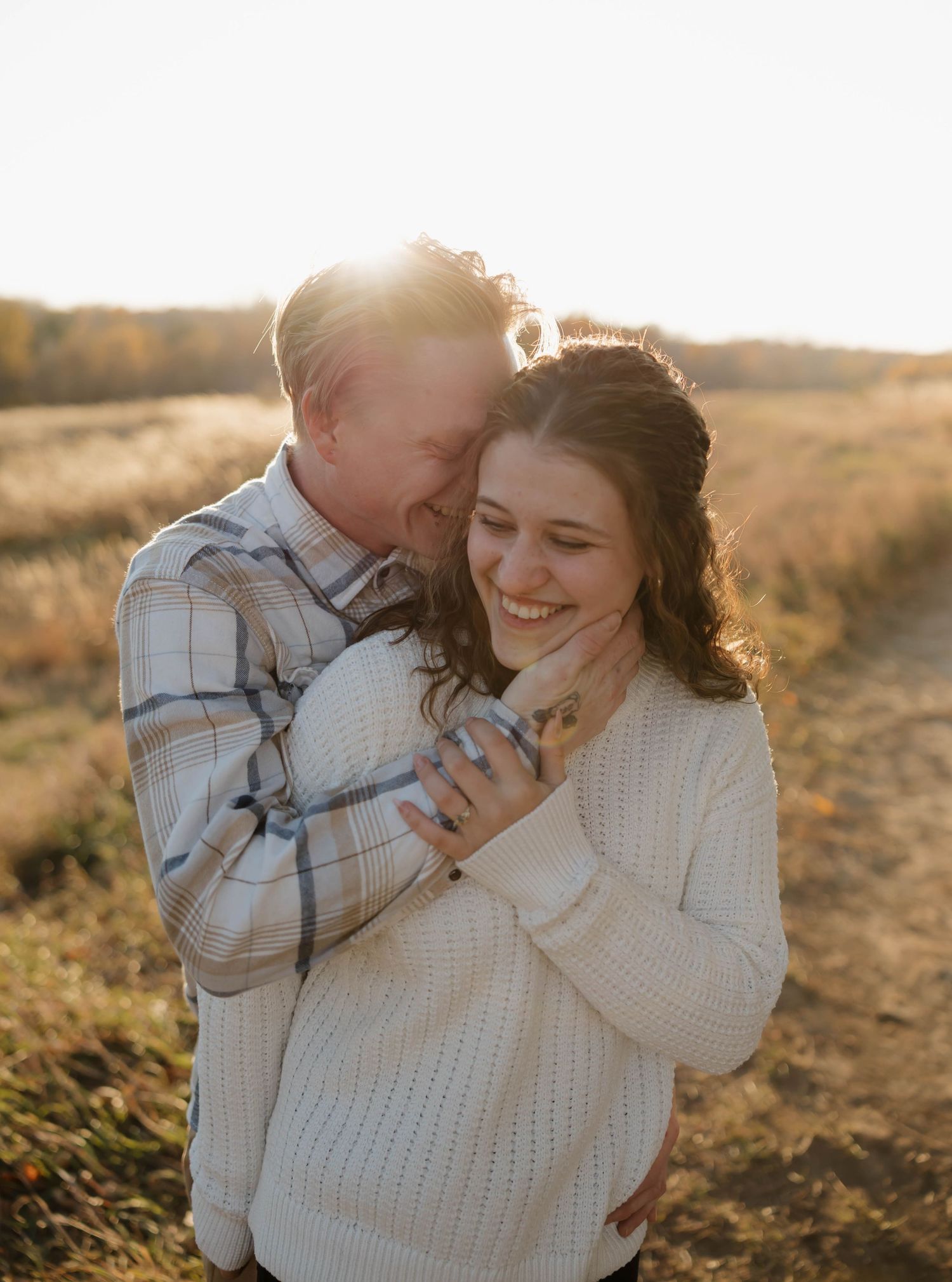 Couple sharing an intimate embrace in a sunlit field during golden hour wearing cozy sweaters.
