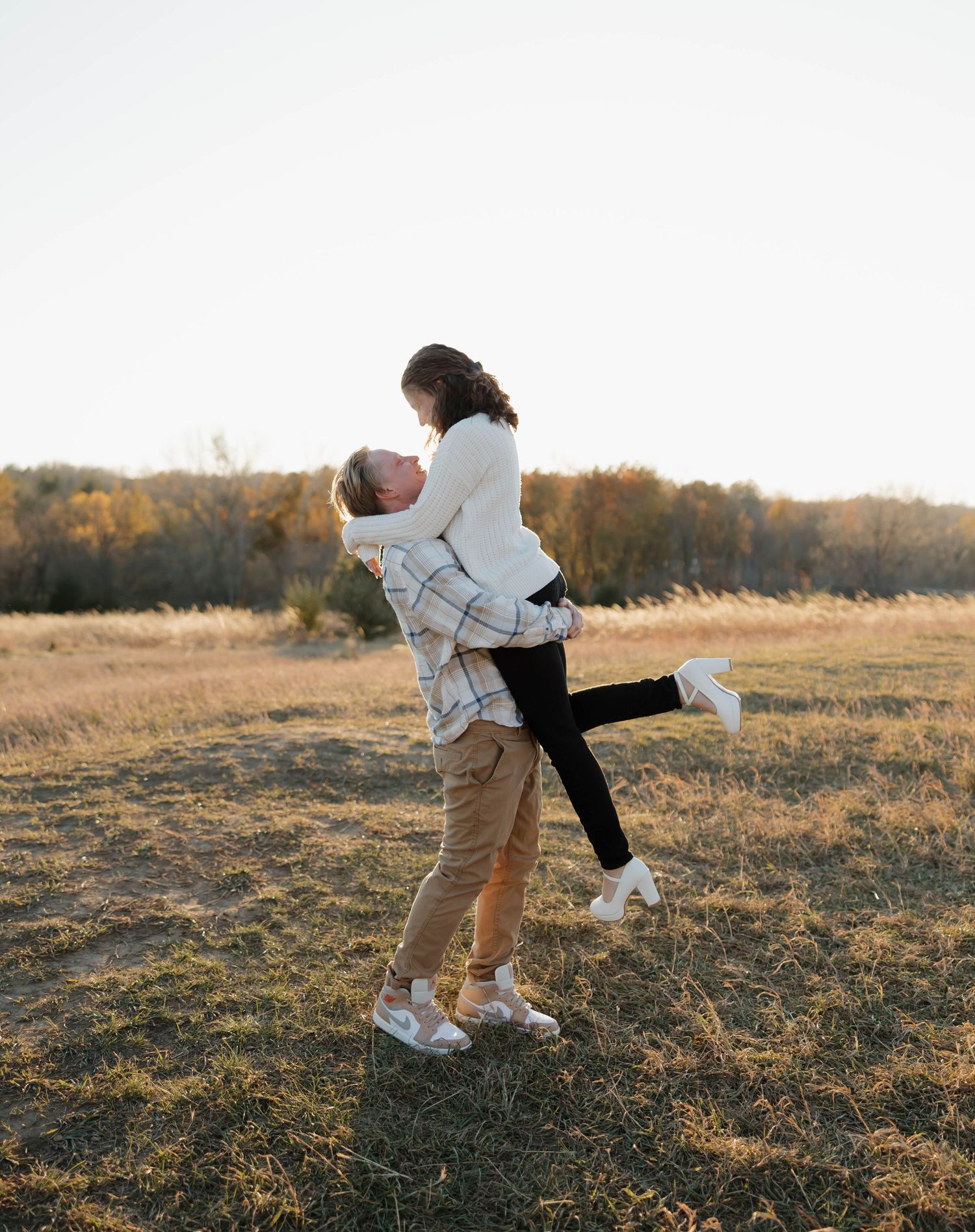 A couple embraces and dances together in a golden sunlit field during sunset.