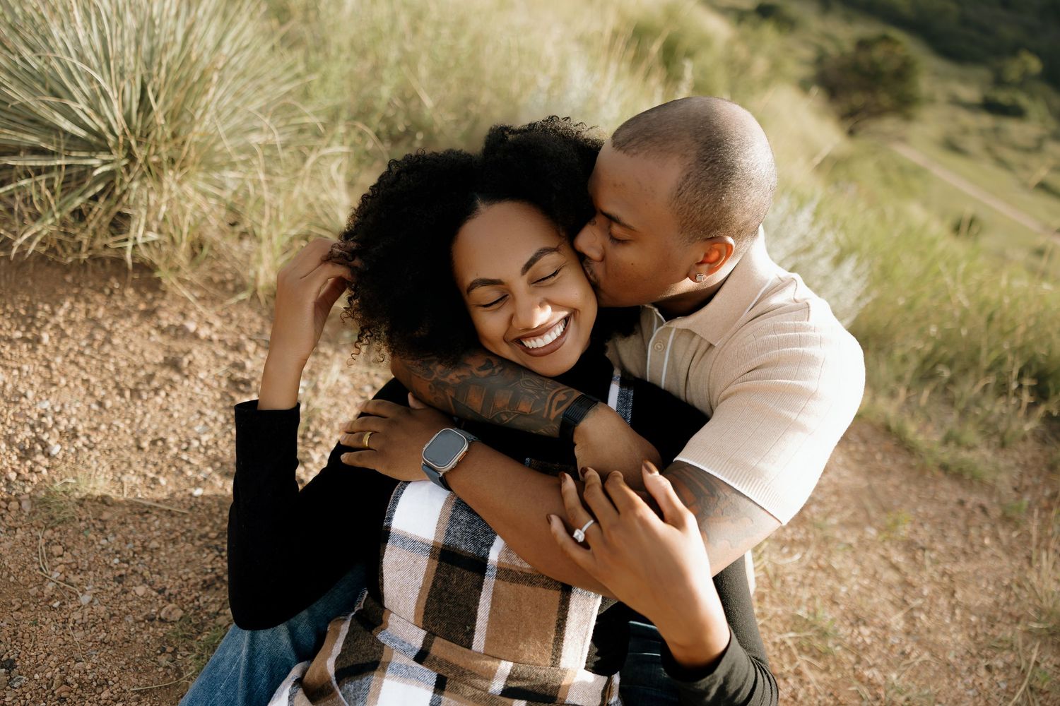 A joyful couple shares tender moments outdoors in a grassy field during a romantic photoshoot session.