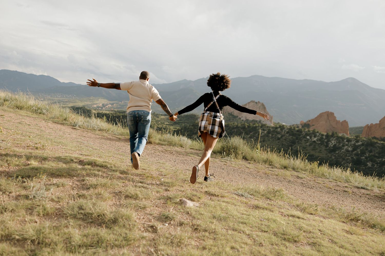 People enjoying outdoor activities on a grassy hillside with mountains in the background on a sunny day.