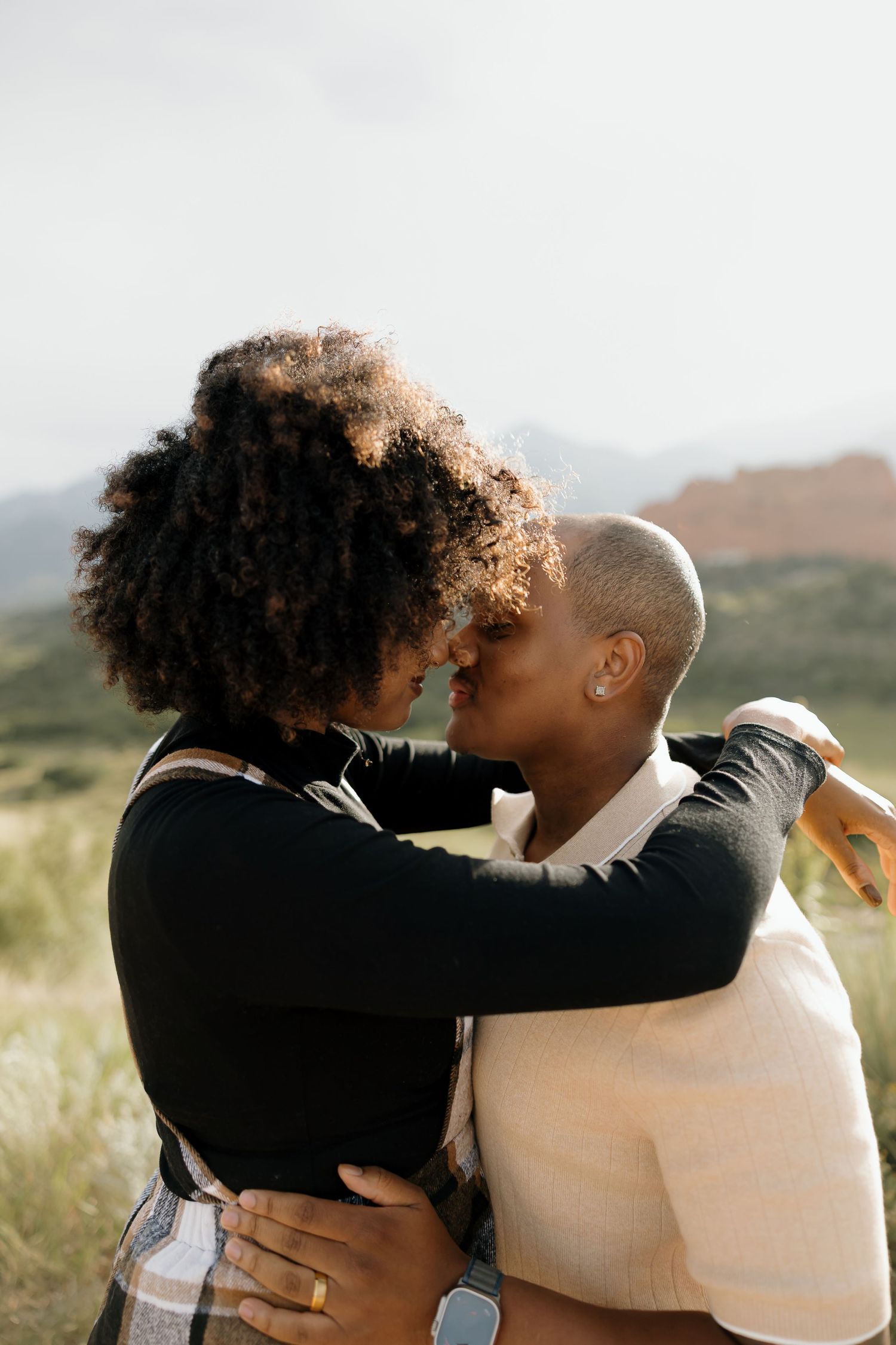 A couple embraces lovingly in a scenic outdoor setting with mountains in the background.