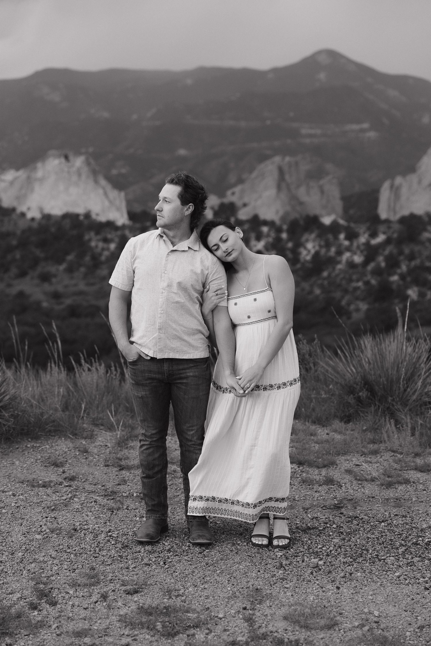 Couple stands at sunset against mountain backdrop in black and white photo series showing casual romantic moments.
