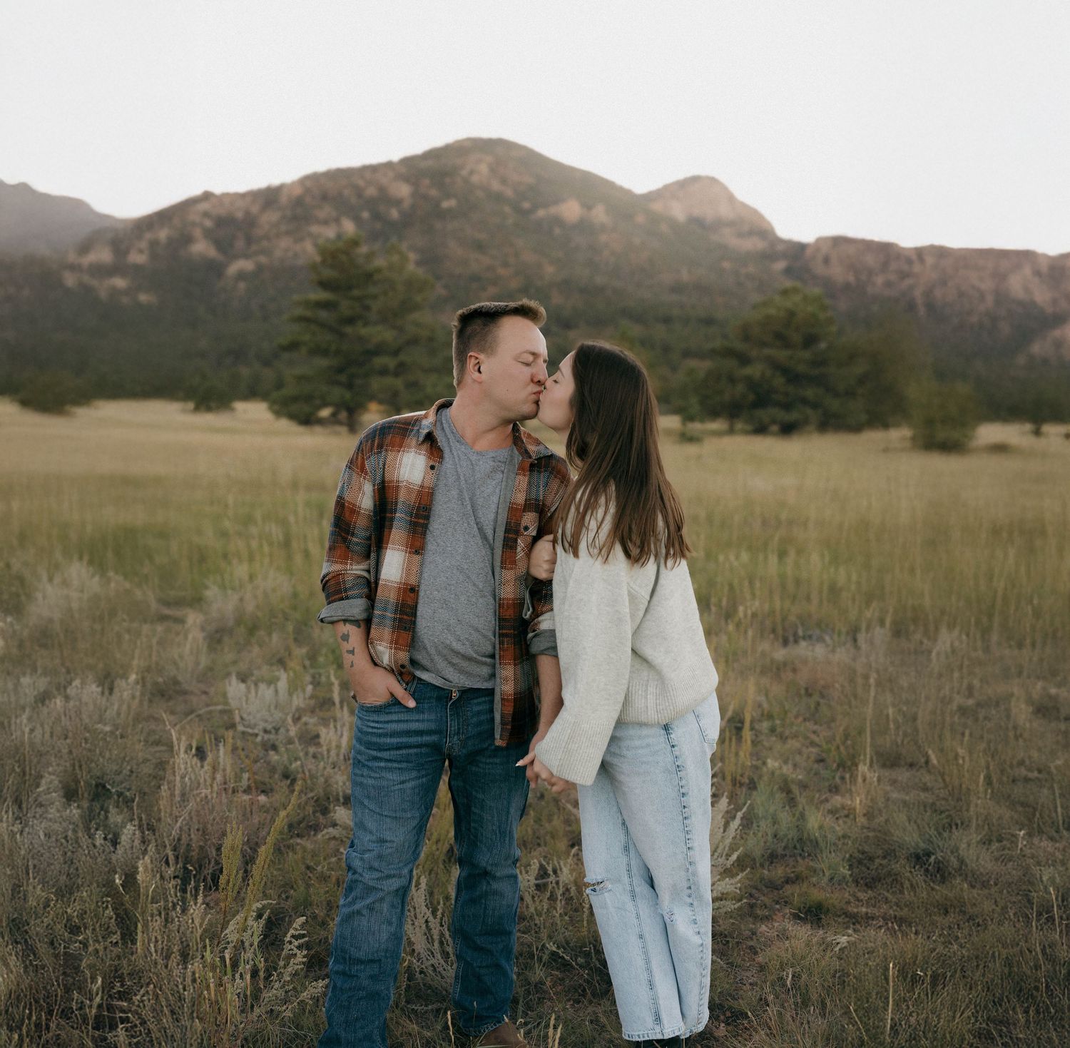 A couple shares an intimate moment together in a field with mountains in the background at sunset.