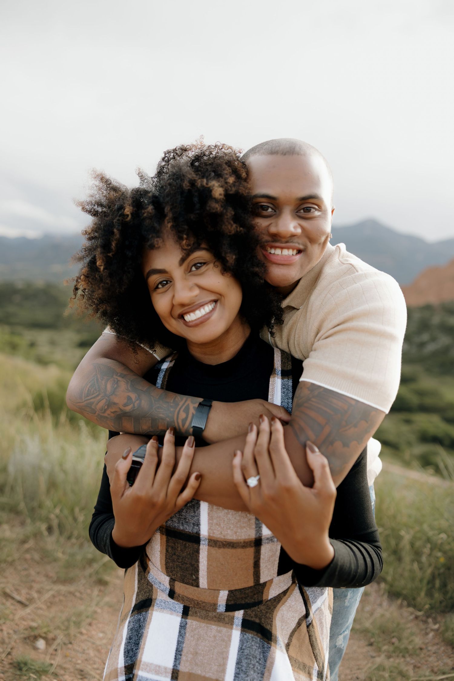 A couple embraces outdoors in a scenic mountain setting while sharing playful and affectionate moments together.