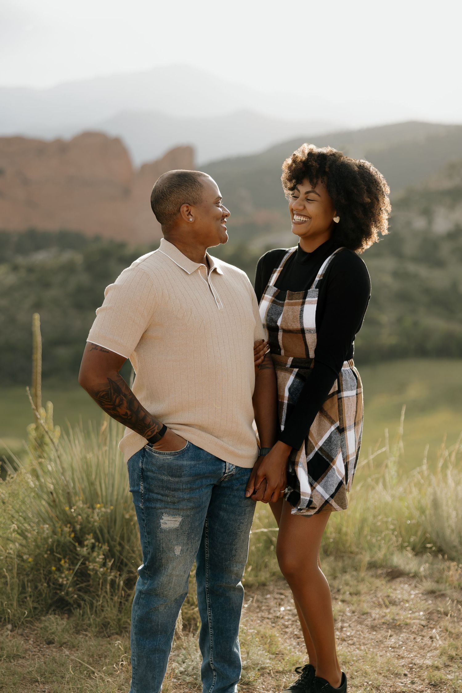 A couple shares a romantic moment together in a scenic outdoor setting with rolling hills in the background.
