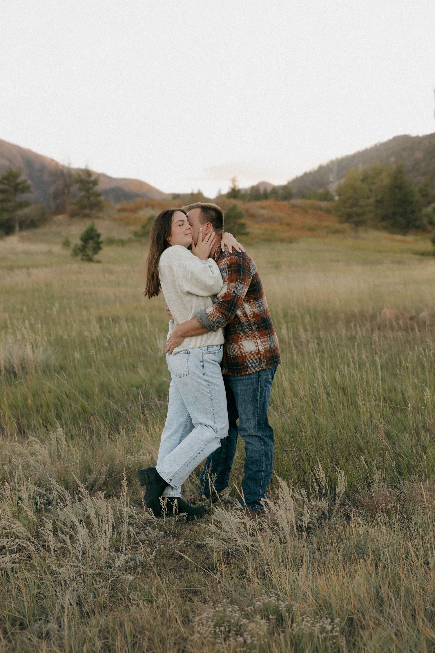 A romantic couple shares an intimate moment in a mountain meadow at sunset.