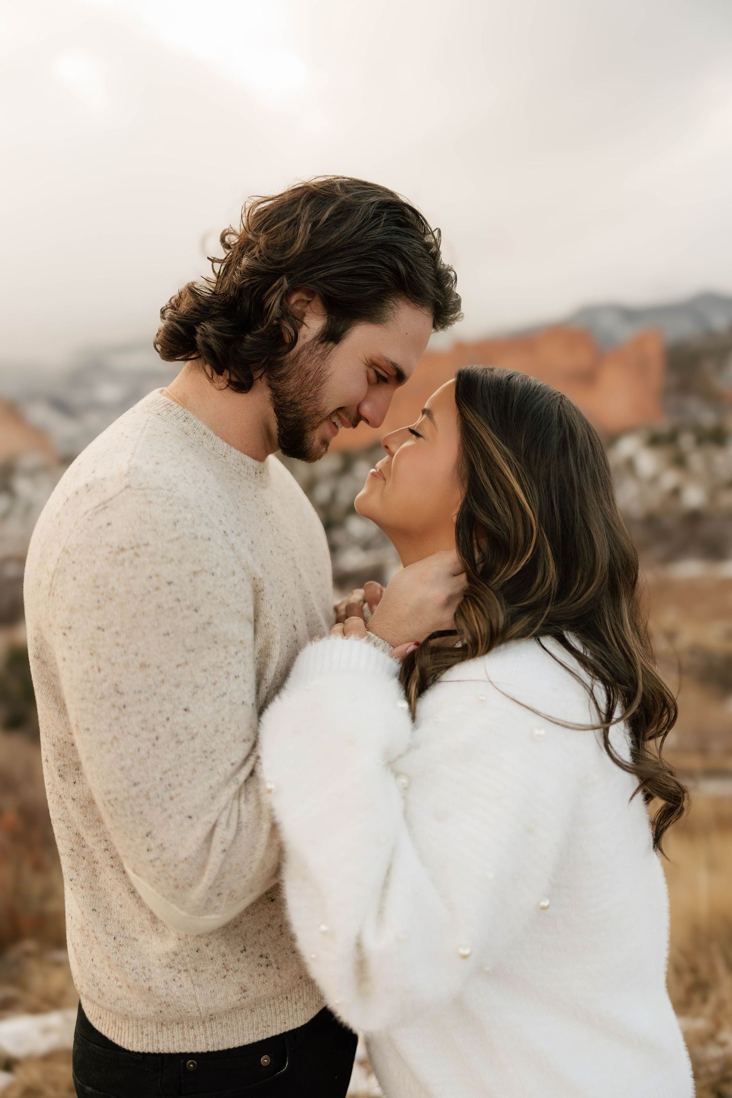 Romantic couple in cozy sweaters share an intimate moment against a misty mountain backdrop during golden hour.