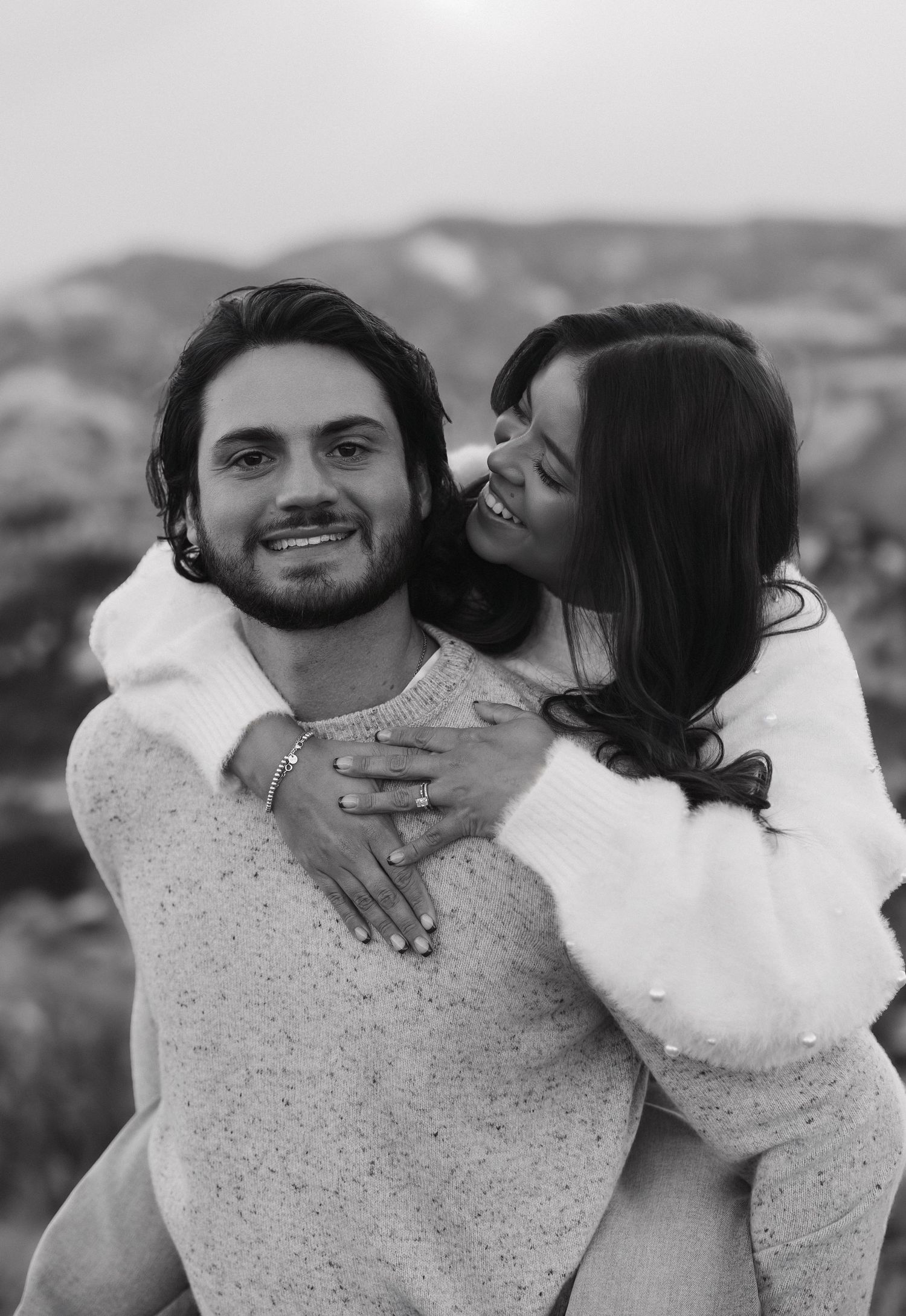 A couple sharing an intimate moment in black and white as they embrace and kiss against a blurred background.